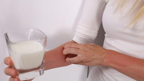 Person with eczema scratching their arm holding a glass of milk