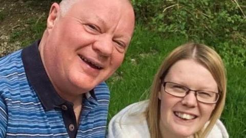 A man in a striped shirt smiles next to his daughter, who wears a grey hoodie.