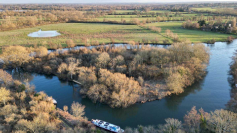 A picture taken on a drone of the wooded island, with woodland and farmland visible in the distance past the Thames.