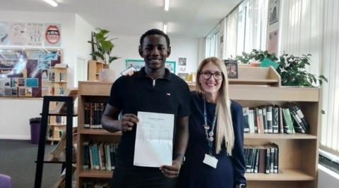 Yusuif poses with his GCSE results alongside the school's principal Claire Stoneman, wearing a blue dress and lanyard, in the library from the previous picture.