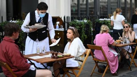 A waiter wearing a mask serves customers sat outside a restaurant in central London, back in September