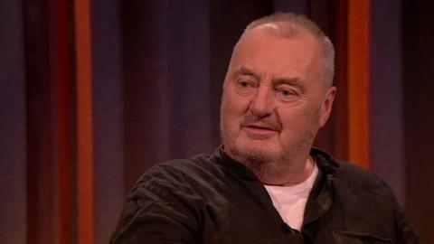 The actor, Jon Kenny seen here on The Tommy Tiernan Show on RTÉ One in June 2019, in a white tee shirt and brown shirt