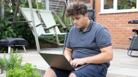 GCSE English literature students uses laptop in the garden for practice quizzes.