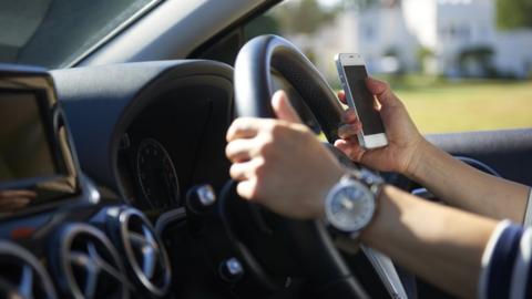 Woman holding mobile phone at wheel of car