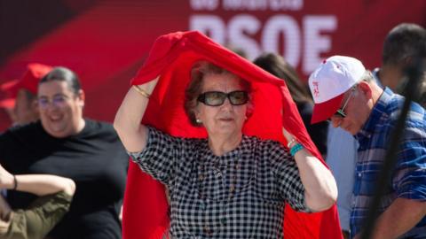 An attendee protects herself from the sun during the presentation of the candidacies for the next elections, at the Fairgrounds, on 11 March, 2023