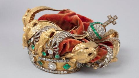 The crown of French Empress Eugenie - a gold crown featuring diamonds, emeralds and golden eagles and a red velvet covering. Its decorations can be seen crushed inwards 