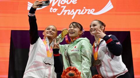 winners of womens floor gymnastics pose for selfie with medals on podium