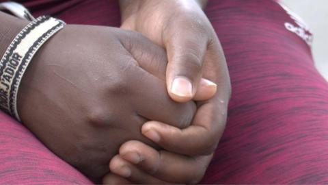 A close-up shot of a Kenyan woman's hands clasped in her lap, in Lebanon