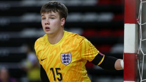 Ben Taylor, a teenager with brown hair, playing futsal in a yellow England shirt