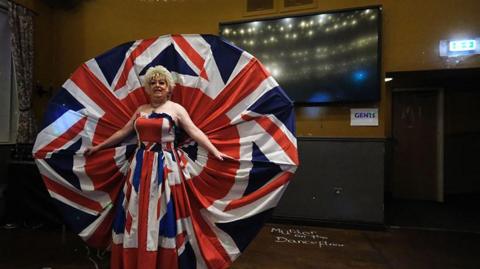 Drag artist Bobby Mandrell in Rayners Pub on Hessle Road  wearing a Union flag outfit that rises up at the back in a circular shape