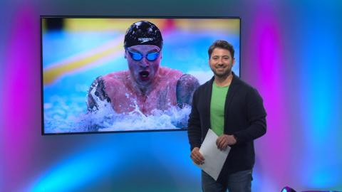 Ricky on the Newsround set with Adam Peaty in the screen