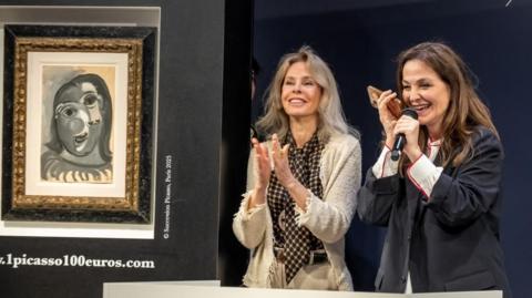 Two auctioneers stand next to a Picasso painting