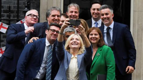 Image shows a group of 11 Mayor's outside number 10 Downing Street taking a selfie.
Former Mayor of Greater Manchester Andy Burnham is to the left of shot wearing a blue suit and striped tie.
The Mayor of West Yorkshire Tracy Brabin is in centre shot, wearing a blue suit and is holding a phone high to take the selfie of all of the mayors.