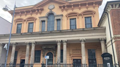 The exterior of a historic Victorian Methodist chapel with ornate columns and an orange frontage. There are large windows on both of the building's two storeys.