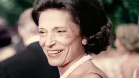 A smiling middle-aged Doris Fisher, with dark brown hair. a white thick necklace, and a black thin strapped dress