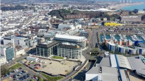 A view of Jersey's financial centre from above. There are large buildings with parking. There is a view of a marina on one side and buildings and trees in the background 