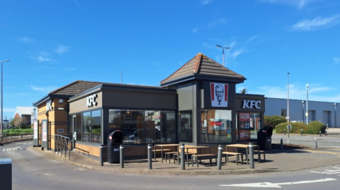 A KFC building with seating outside and bollards.