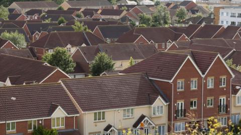 A drone image of a housing estate. The aerial image shows the tightly-packed rooves of a housing development stretching into the distance.