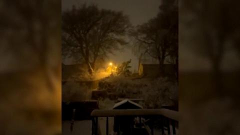A view of snow at night from a window during a thunderstorm