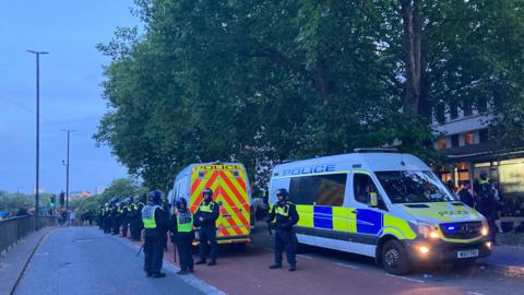 Police lined up on bridge with several riot vans