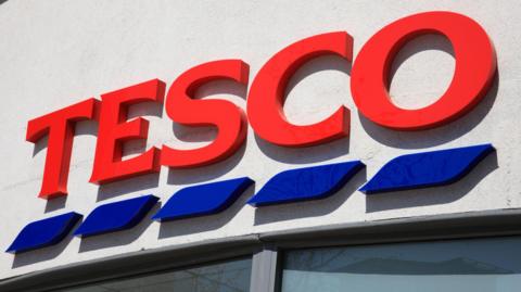 A red and blue Tesco sign on a wall above a window.