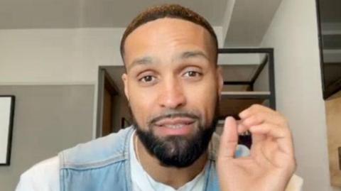 Ashley Banjo doing an OK sign to a camera mid-speech