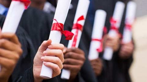 A close up image of the hands of of university graduates in a line holding diploma scrolls. 