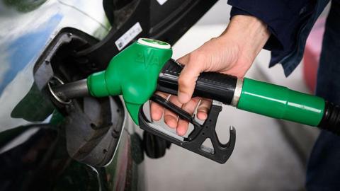 A person fills up their car with a petrol pump. 