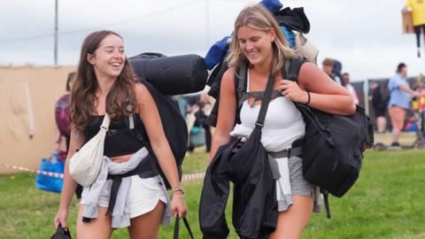Two women walking into a festival carrying equipment