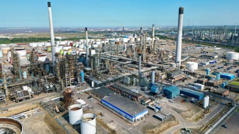 A drone view of the Prax Lindsey Oil Refinery. A cluster of metal structures rising to the blue sky.