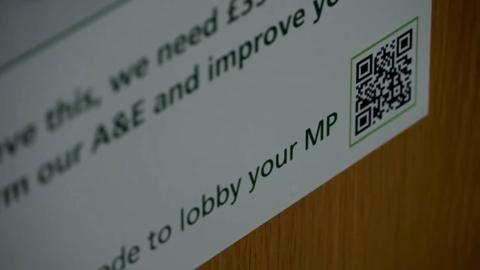 A close up shot of a QR code poster on a wooden door with some words out of focus and 'to lobby your MP' in focus.