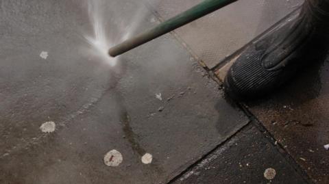 A jet washer spraying the pavement that has chewing gum stuck on it
