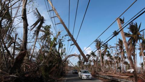 A car drives under a broken power pole