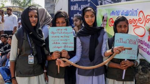 Students hold placards and a toy snake during a protest over the death of a girl after she was bitten by a snake inside her classroom at Sulthan Bathery