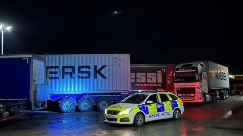 Police car in front of lorries at night