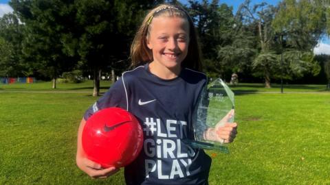 Lola holding her football and Let Girls Play award