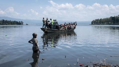 A little boy watches a boat with many people sail off