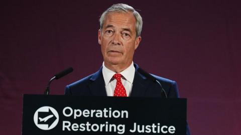 Nigel Farage, who has short grey hair parted to the side speaks at a podium with the words Operation Restoring Justice on it. He is wearing a dark suit, white shirt and red spotted tie.
