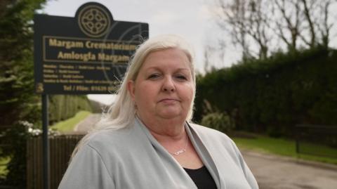 A woman with blonde hair in front of a dark sign