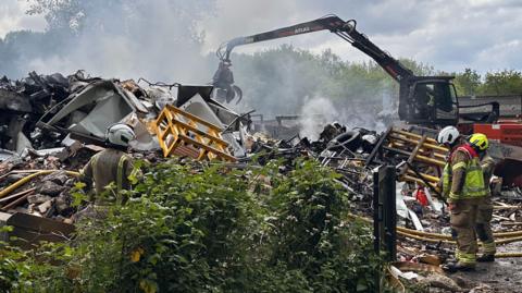 A close up of the firefighters inspecting the scrap metal that is alight. Hoses used to tackle the blaze remain on the ground. 