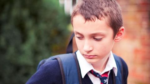 Young boy in his school uniform and school bag on his back.