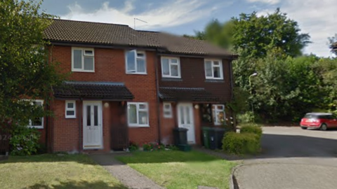 A two-storey, end-of-terrace house with a lawn in front and a small car park beside it.