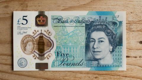 New five pound note on a wooden kitchen table background with Queen's head visible
