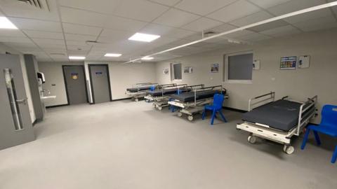 The new lounge it has grey walls and dark grey doors and a number of beds with blue chairs next to them