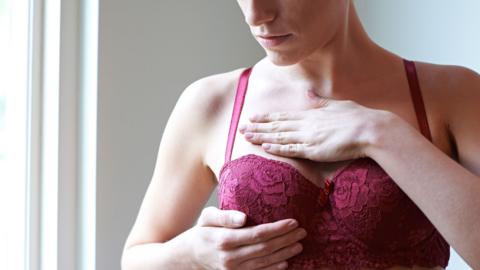 A woman wearing a bra examining her breast