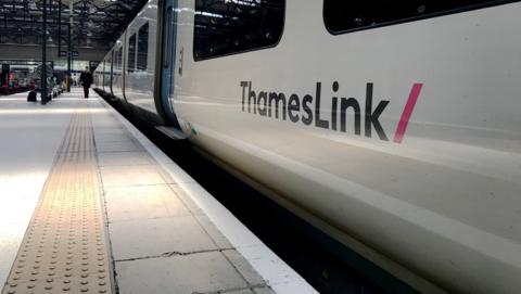 A Thameslink train at a station platform. There is a guard walking towards the camera in the distance.
