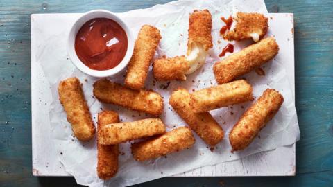 Mozzarella sticks on baking sheet, with a red dip beside.