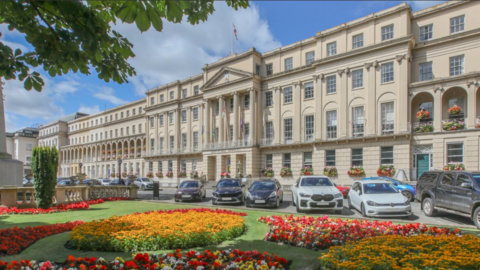 The exterior of the grand regency building that houses Cheltenham Borough Council. It is a bright sunny day and there are thriving red and orange flower beds at the front of the building