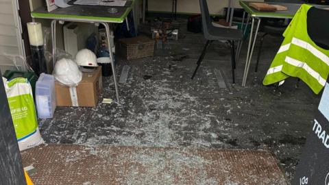 Shattered glass on the floor of a room with builders' equipment including hi-vis jackets and helmets