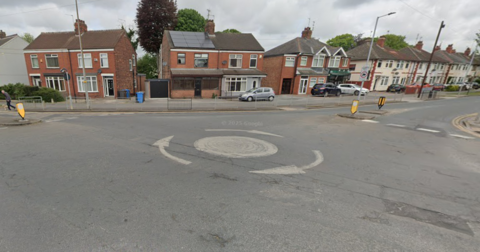 Google view of the roundabout at the junction of James Reckitt Avenue and Gillshill Road. There are white circular markings in the centre of the image with arrows pointing clockwise. There is a row of houses in the background. 